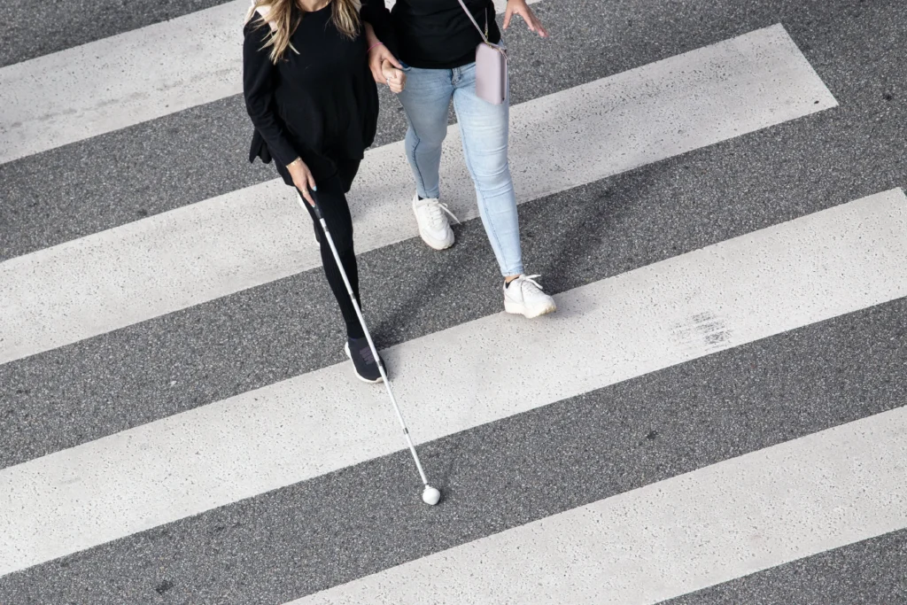 student needs an orientation and mobility specialist. Woman helping a female student with a cane to cross the street.